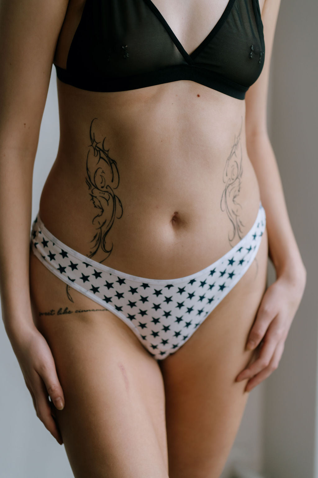 Person wearing a black bikini top and white underwear with star pattern on a neutral background